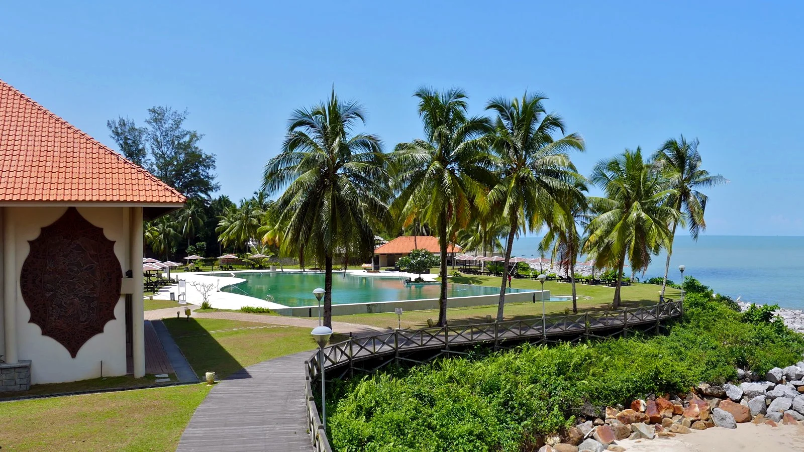 The pool terrace at Damai Beach Resort, with coconut palms and the sea beyond